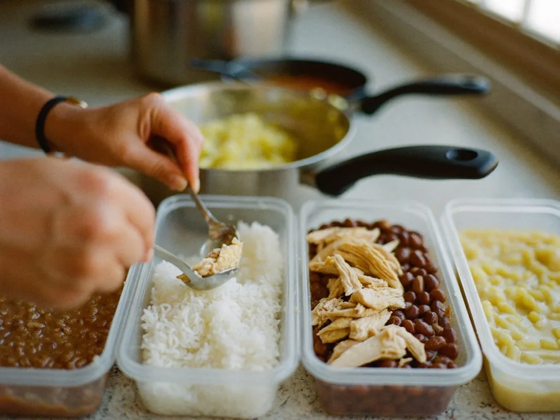 Marmitas sendo porcionadas com arroz, feijão e frango